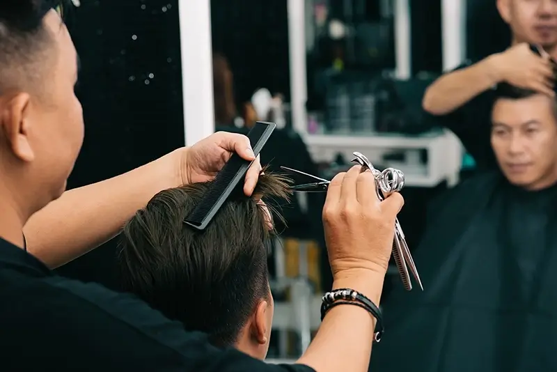 male-hairdresser-cutting-customer-s-hair-with-comp-scissors-front-mirror